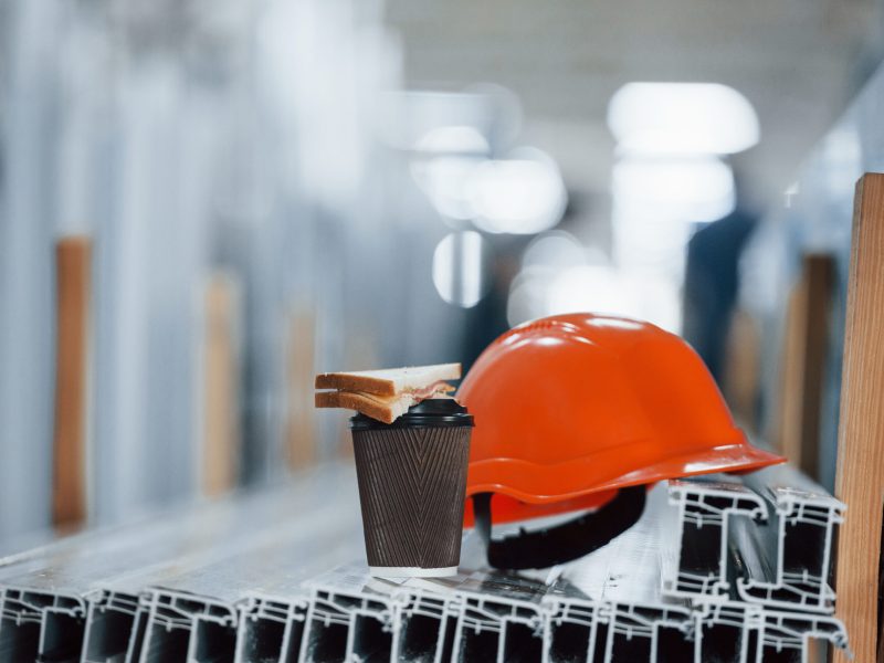Bread is on the cup with drink. Orange hard hat on objects in the factory. No people. Conception of lunch break.